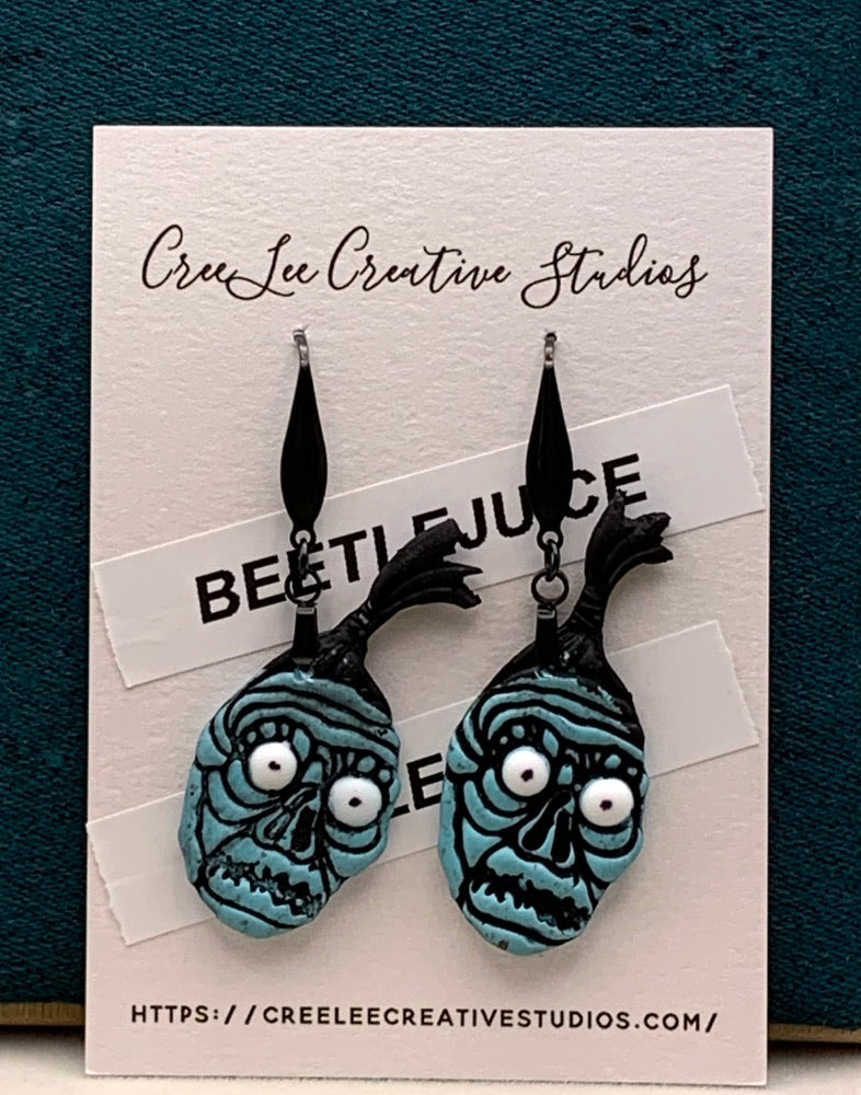 A pair of blue earrings designed to resemble the character BOB the Shrinker from the Beetlejuice movie, displayed on a card with the brand CreeLee Creative Studios.