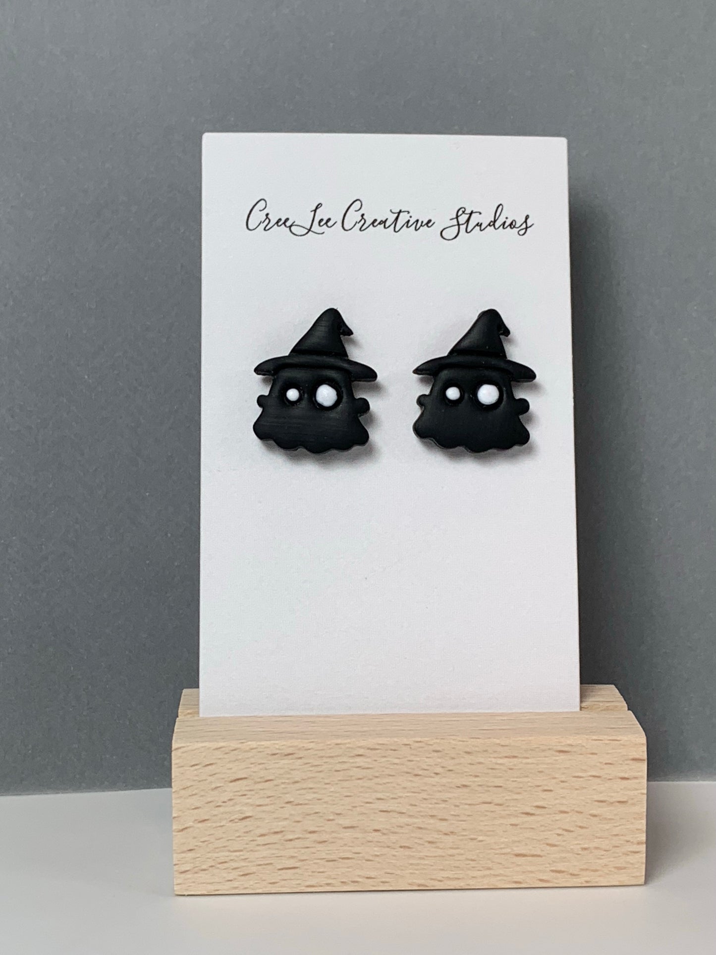 A black ghost with black hat stud earring on a business card in a wooden stand.