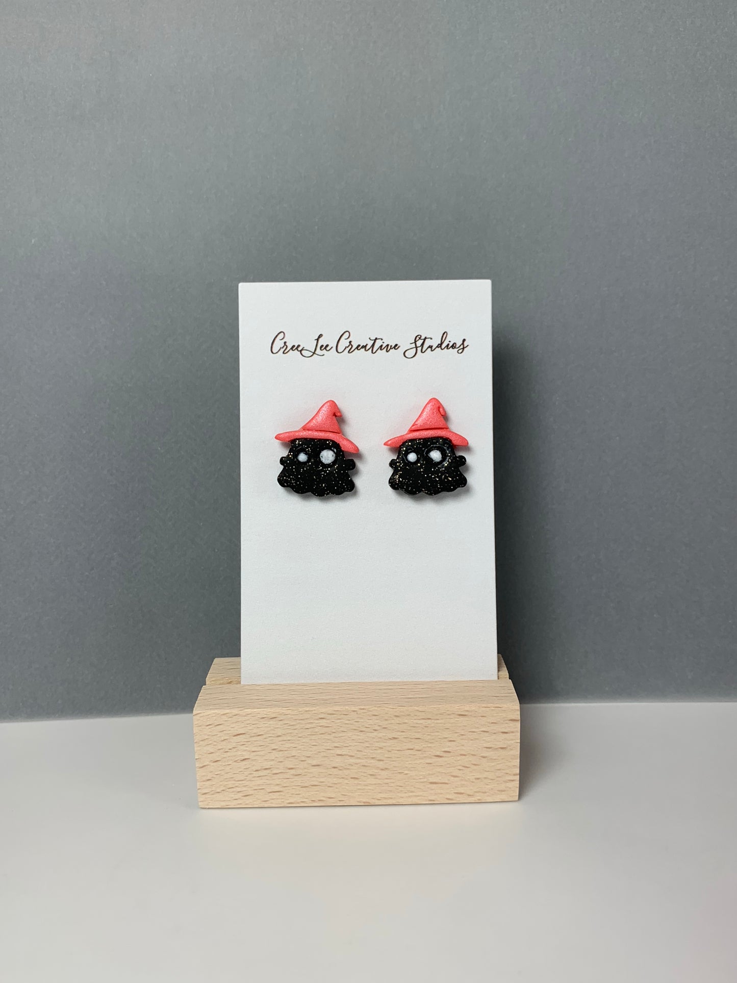 A sparkle black ghost with coral hat stud earring on a business card in a wooden stand.