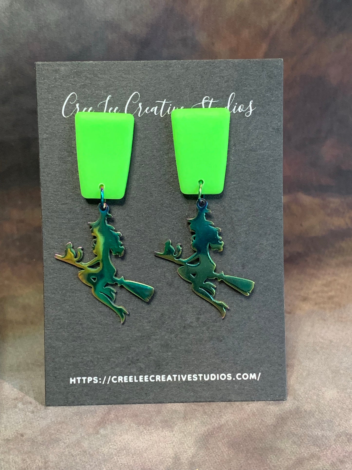 A pair of vibrant neon green dangle earrings with a stainless steel witch charm.