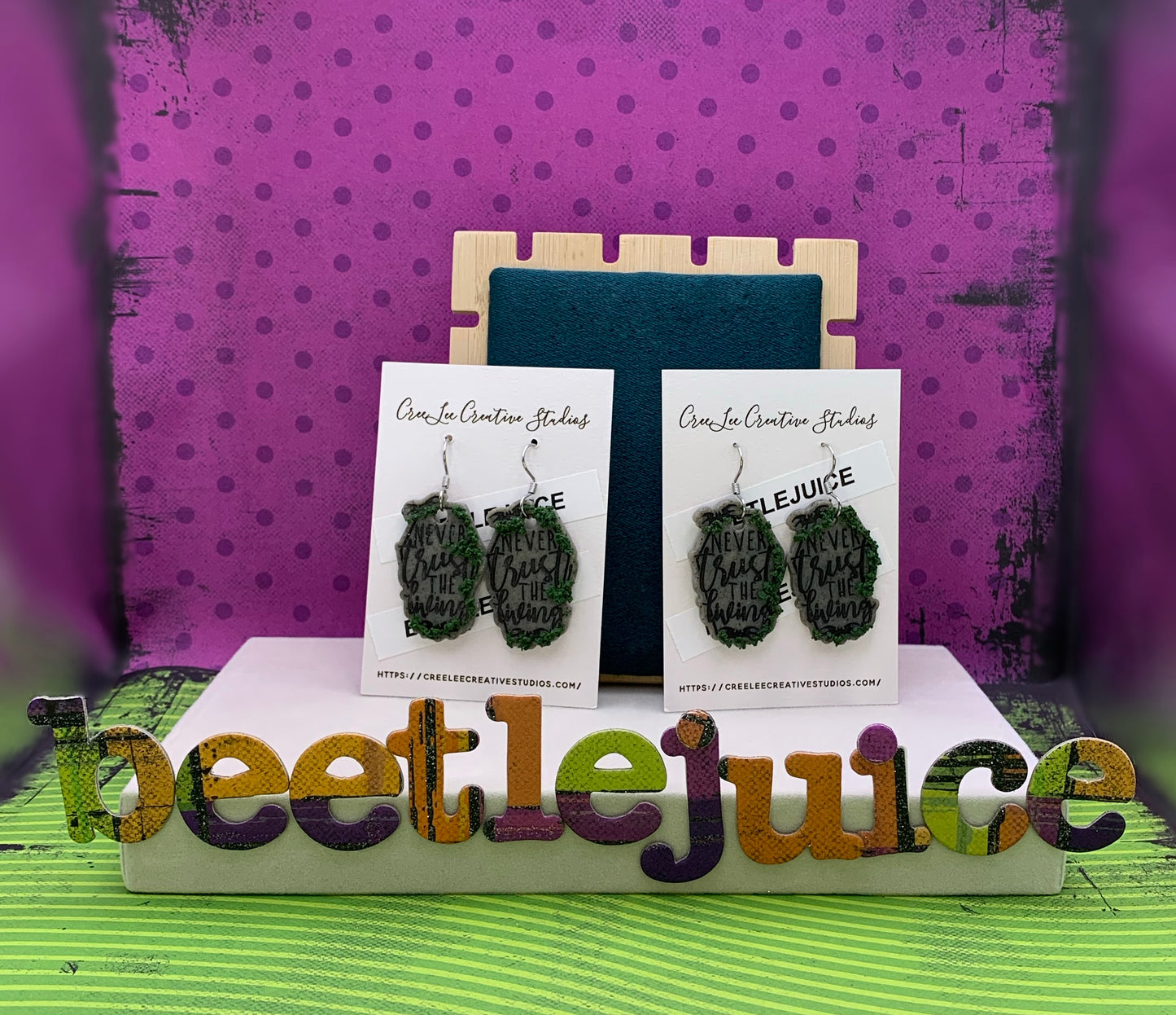 Never Trust the Living Tombstone with Growing Moss Earrings with a purple polka dot and green stripped background