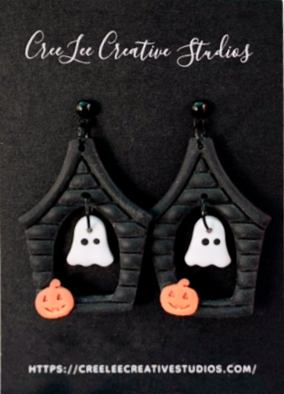 Halloween-themed earrings with haunted house design on a black card with brand name.