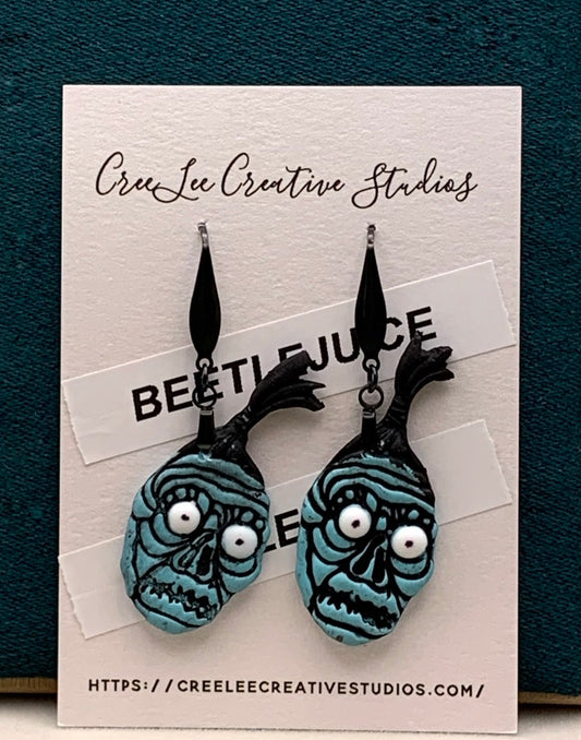 A pair of blue earrings designed to resemble the character BOB the Shrinker from the Beetlejuice movie, displayed on a card with the brand CreeLee Creative Studios.