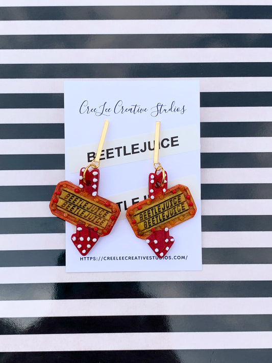 A pair of red and yellow 3D earrings with 'BEETLEJUICE' text and a flashing sign design.
