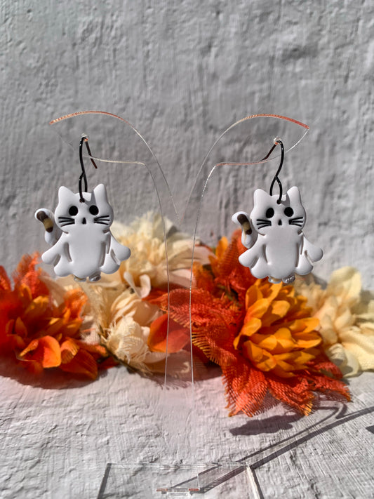 Handmade Calico Cat Ghost Dangle Earrings — spooky-cute polymer clay earrings that blend calico cat charm with ghostly whimsy. Each lightweight dangle features a white ghost-cat silhouette with minimalist black eyes, whisker detail, and a small calico-patterned tail; finished on black-plated fishhook findings for an on-trend, edgy look. Perfect for shoppers searching for cat ghost earrings, calico cat jewelry, polymer clay Halloween earrings, kawaii cat earrings, or handmade spooky-cute accessories. 