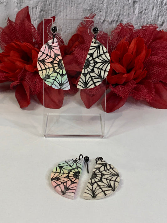 Handmade Spiderweb Dorm Window Earrings — mismatched polymer clay dangles inspired by the iconic Nevermore Academy dorm room window from Wednesday. One half is a soft pastel rainbow spiderweb, the other a stark black-and-white half; together they form a full round dorm window. Perfect for Wednesday Addams earrings, Nevermore Academy jewelry, mismatched spiderweb earrings