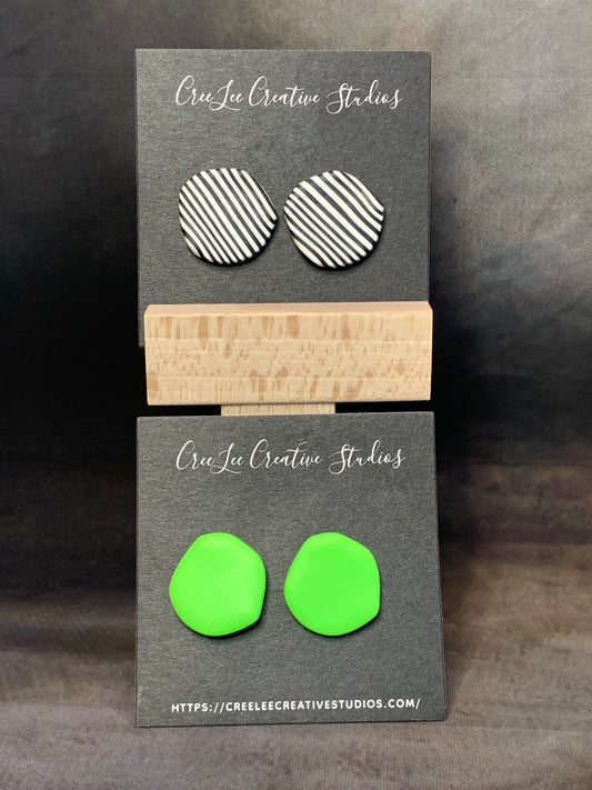 The image shows two pairs of earrings designed with large, abstract circles. One pair has black and white stripes, tje ptjer is neon green and both are displayed on a card with the brand name 'CreeLee Creative Studios'.