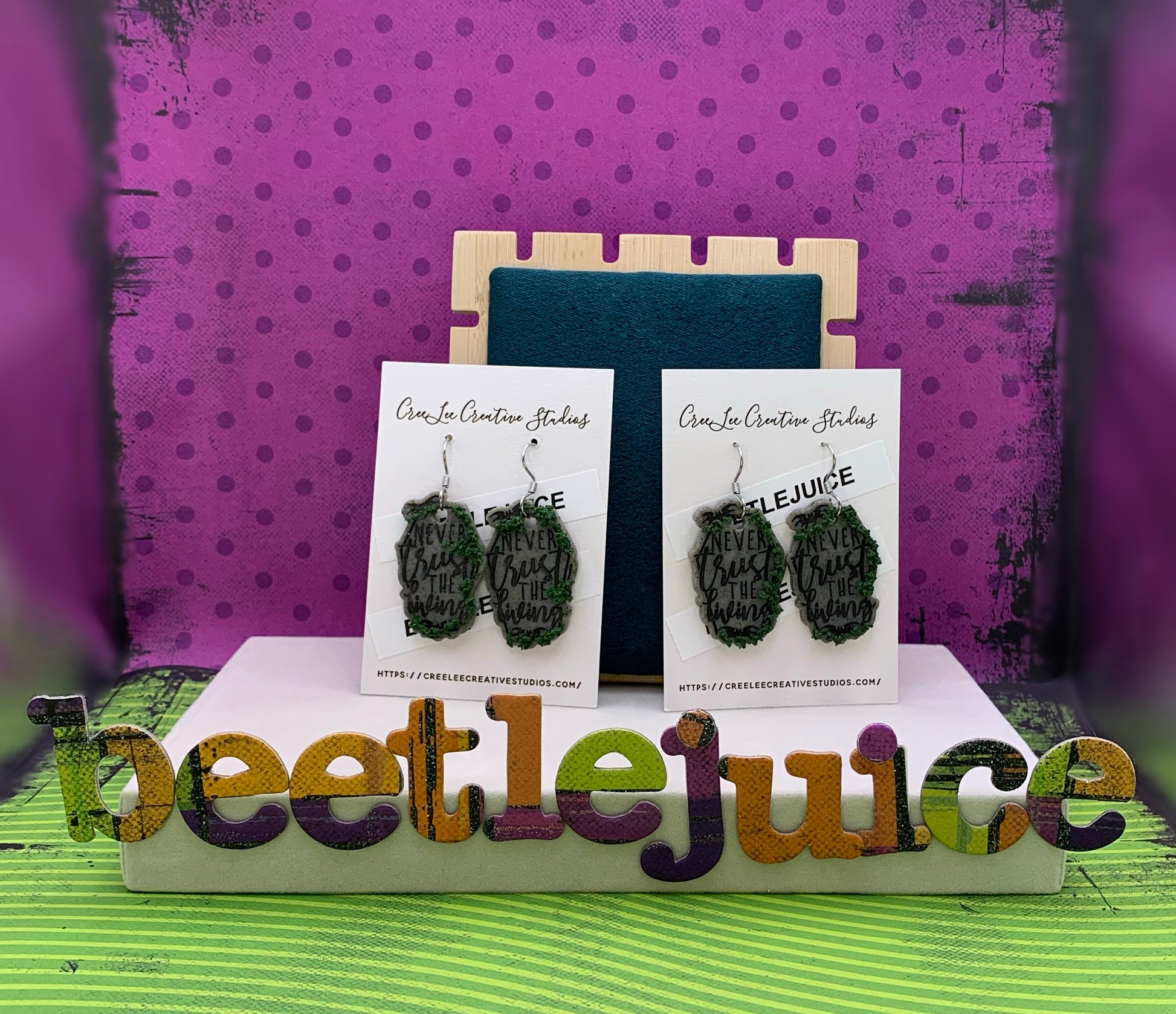 Never Trust the Living Tombstone with Growing Moss Earrings with a purple polka dot and green stripped background