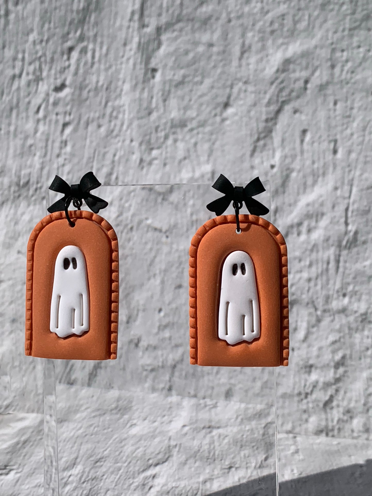 Handmade Orange Ghost Arch Earrings — statement polymer clay earrings featuring a white ghost with black eyes set in a pumpkin-orange arch with stitched detailing, topped by a chic black bow finding.