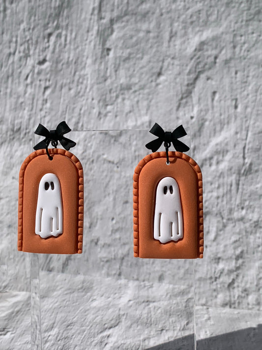 Handmade Orange Ghost Arch Earrings — statement polymer clay earrings featuring a white ghost with black eyes set in a pumpkin-orange arch with stitched detailing, topped by a chic black bow finding.