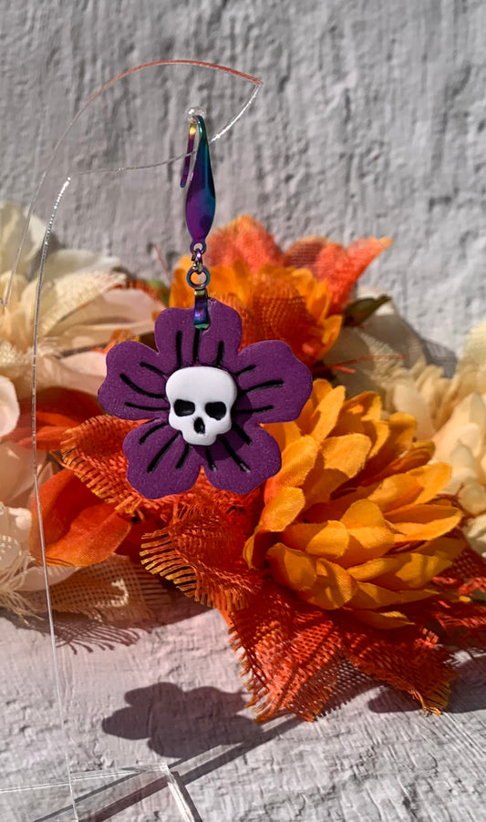 Purple flower-shaped earring with a skull design on a floral background