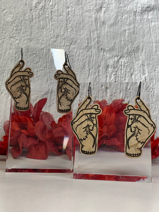 Handmade “Thing” Snapping Earrings — an iconic nod to Wednesday Addams and the Addams Family. These lightweight, hand-cut polymer clay dangles (available in multiple skin tones) feature high-contrast engraved/inked linework that captures Thing’s snap pose with stitched-wrist detailing. Perfect for Addams Family jewelry, Wednesday Addams earrings, gothic Halloween earrings
